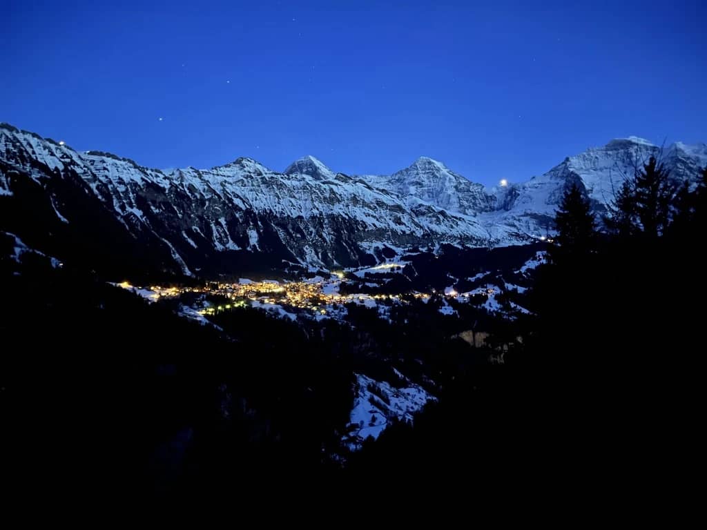 Evening lights of the Lauterbrunnen valley glow below snowy peaks seen from the slopes around Isenfluh