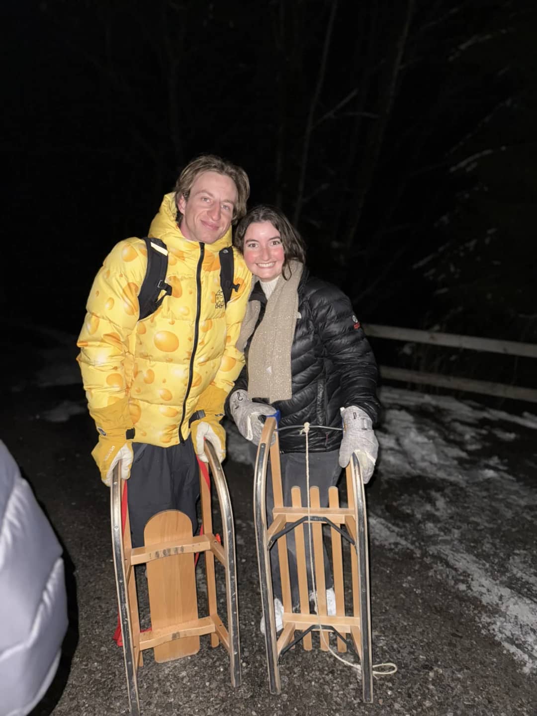 Two sledders hold wooden toboggans in Isenfluh village at night after a headlamp run down from Sulwald forest