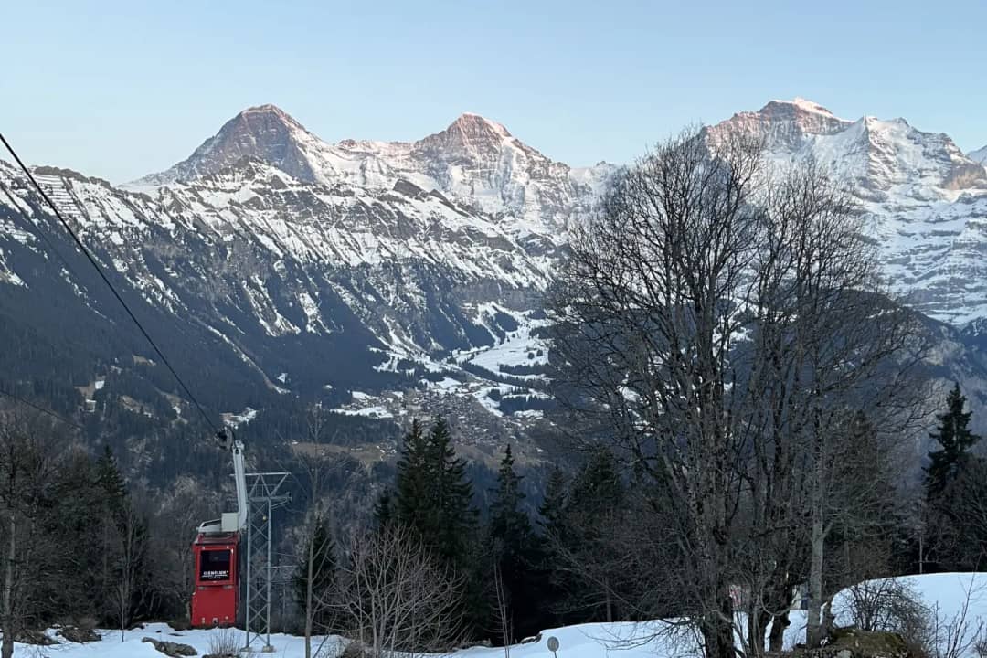 The small red Isenfluh cable car cabin above snowy meadows, with the Jungfrau across the Lauterbrunnen valley