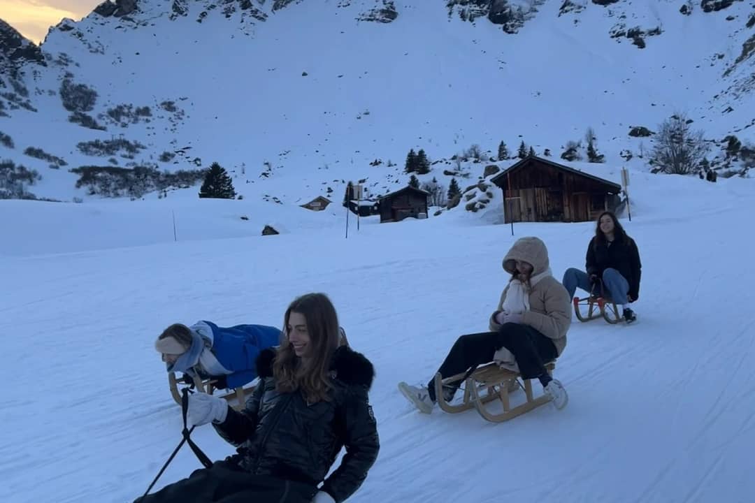 Amigos bajan en trineos de madera por una ladera nevada y soleada sobre Mürren en febrero, desde Interlaken