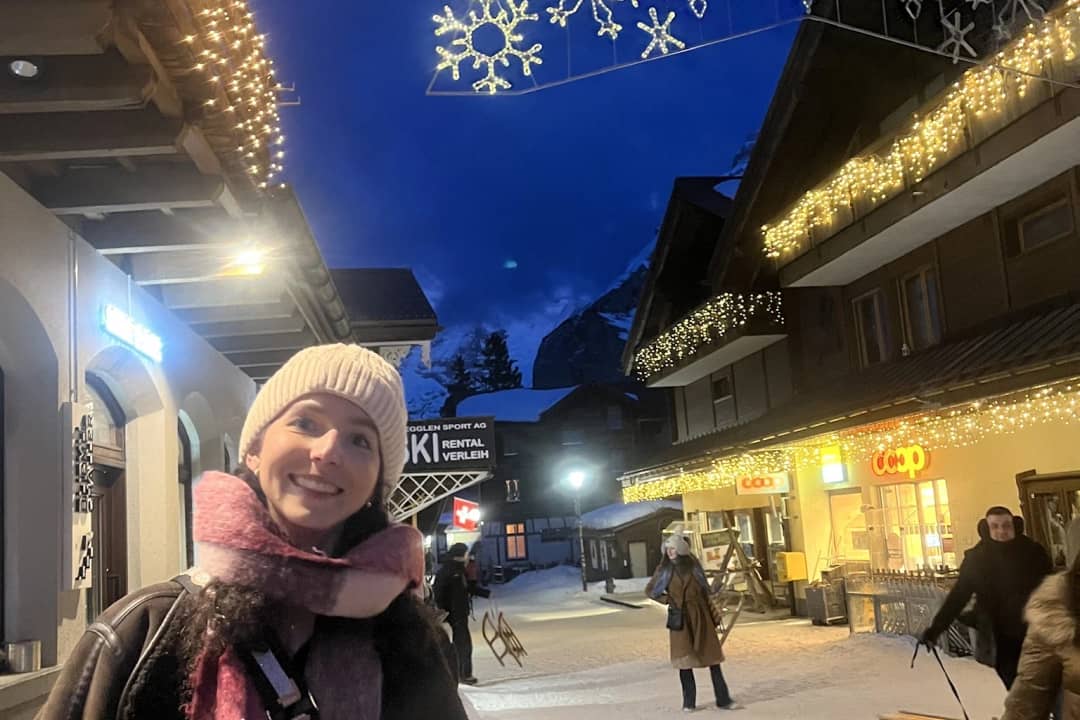Una visitante sonriente pasea al anochecer por Mürren, sin coches, bajo las luces de Navidad y con nieve
