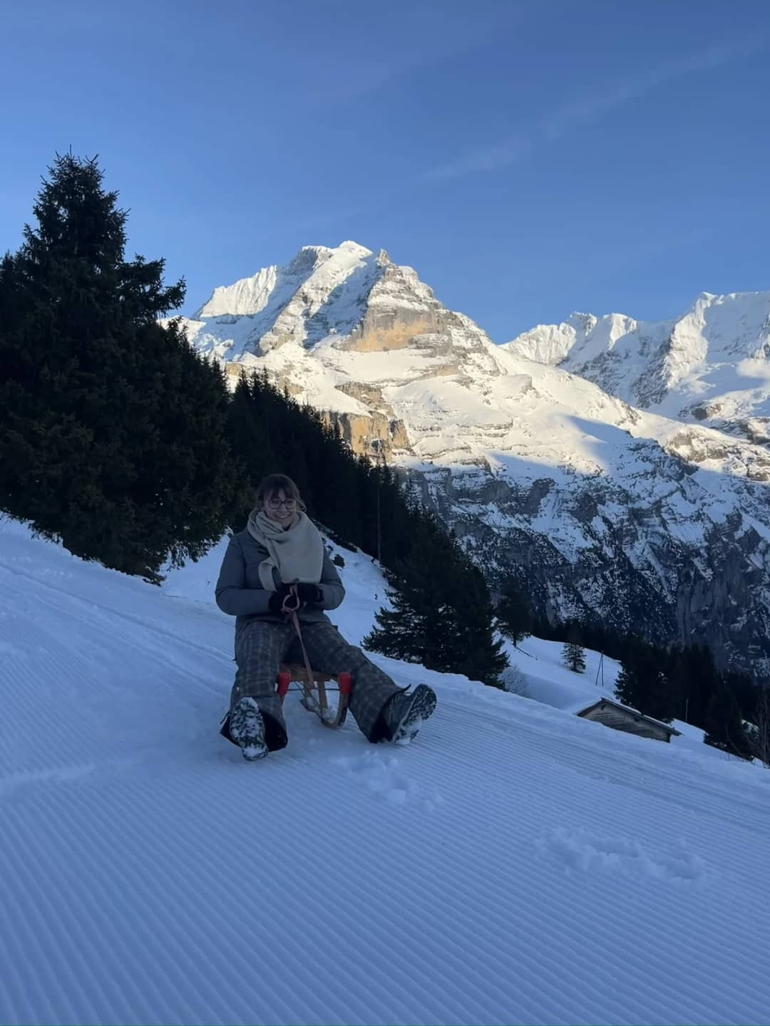 Sledding in Switzerland: a rider on a groomed slope above Mürren in the evening, below sunlit snowy peaks