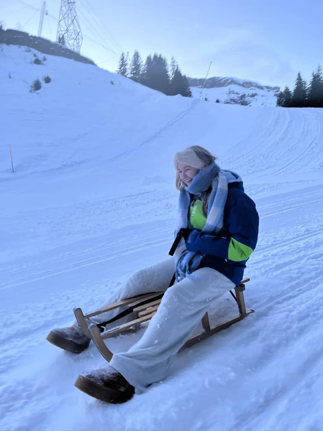 A woman brakes with both heels in the snow on a wooden sled above Mürren, showing how to brake on a sled