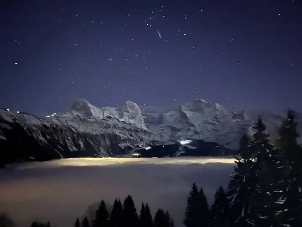 Snowy peaks under a starry sky above a glowing sea of fog, seen from the night sledding run at Isenfluh