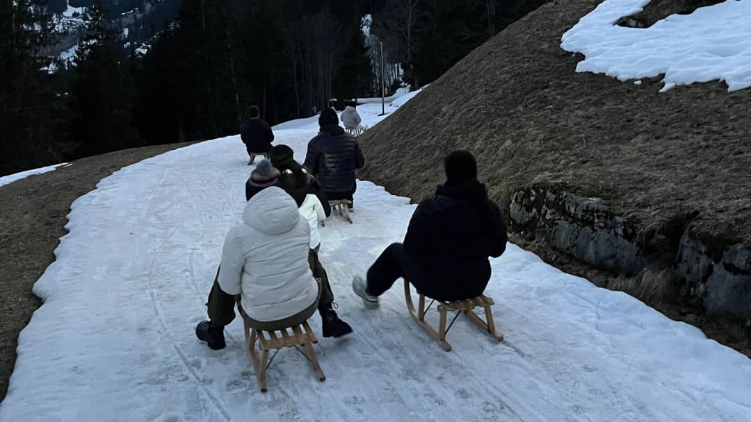 Sledders ride down the snowy forest road from Sulwald towards Isenfluh at dusk on a night sledding tour