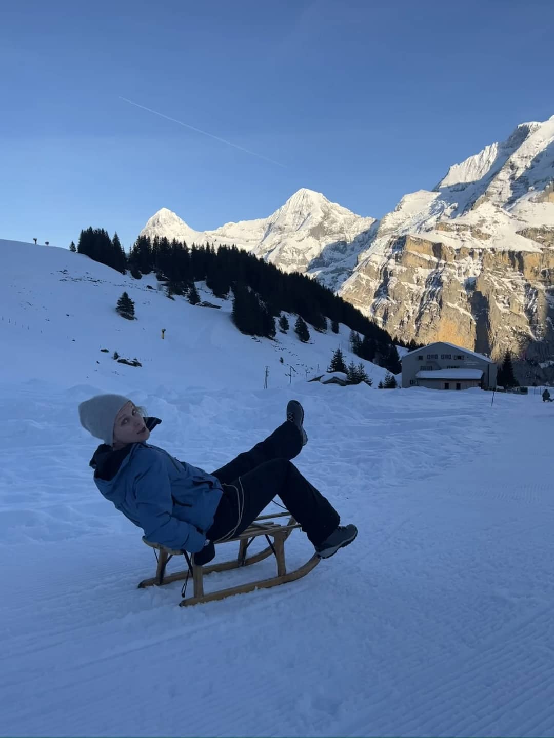 A sledder leans back on a wooden sled on the Bob Run above Mürren as the evening sun lights the peaks behind