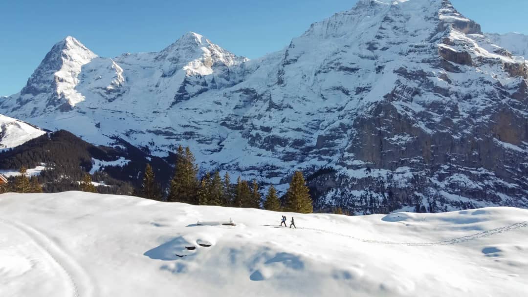 Dos personas con raquetas cruzan el Chänelegg Trail sobre Mürren bajo el Eiger y el Mönch, en Interlaken