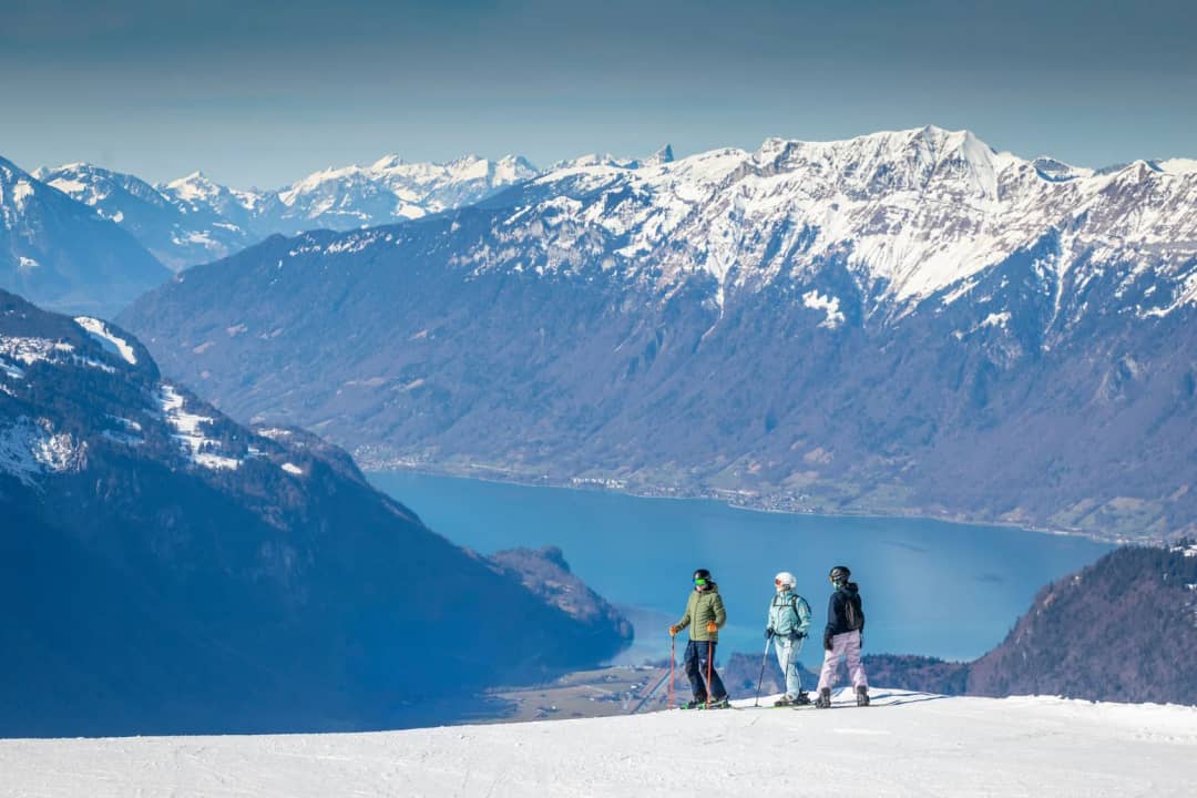 Drei Skifahrer halten auf einer Piste von Meiringen-Hasliberg, tief unten der Brienzersee, Skigebiet Hasliberg