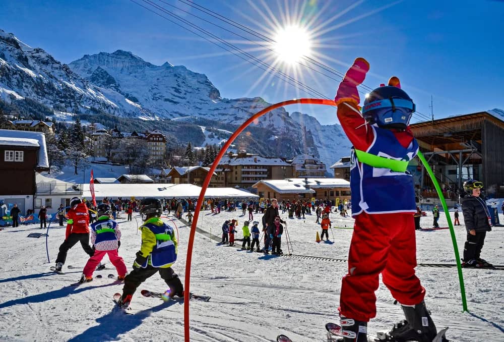 Kinder einer Skischulklasse folgen ihrem Skilehrer auf dem flachen Anfängerhang in Wengen im Winter, Skikurs