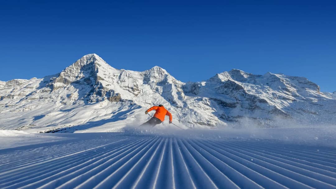 Ein Skifahrer in Orange auf einer präparierten Piste an der Kleinen Scheidegg, Skifahren bei Interlaken