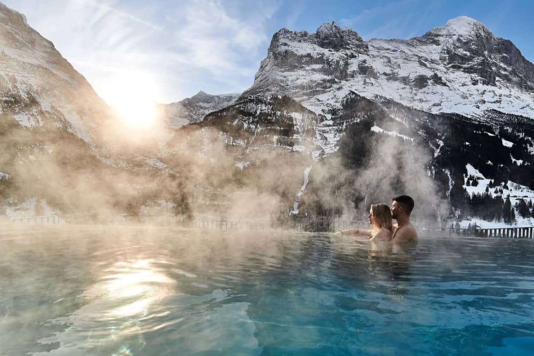 Ein Paar im dampfenden beheizten Aussenpool in Grindelwald vor dem verschneiten Eiger, Spa statt Skitag