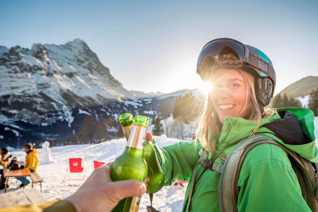 Zwei Wintersportler stossen in der tiefen Sonne an Grindelwald-First vor dem Eiger an, Ende eines Skitags