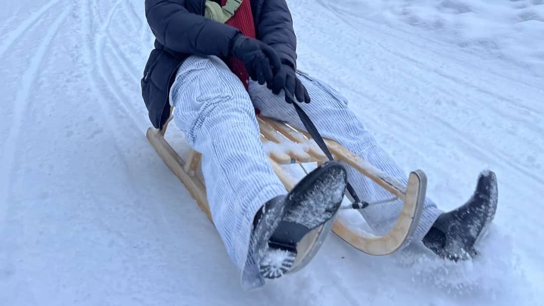 What to wear sledding in Switzerland: gloves, a puffer jacket and winter boots on a wooden sled above Mürren