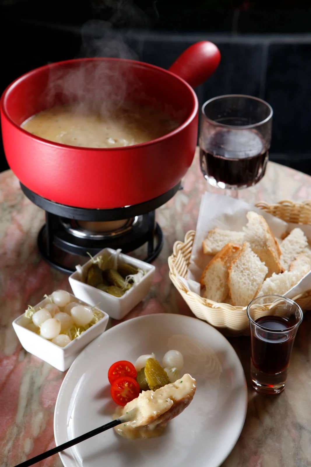 Fondue au fromage dans un caquelon rouge avec pain, oignons et cornichons : ce que comprend le prix d'une fondue