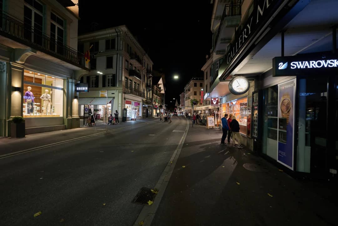 Le Höheweg à Interlaken le soir, vitrines éclairées le long de la rue où les visiteurs cherchent une fondue