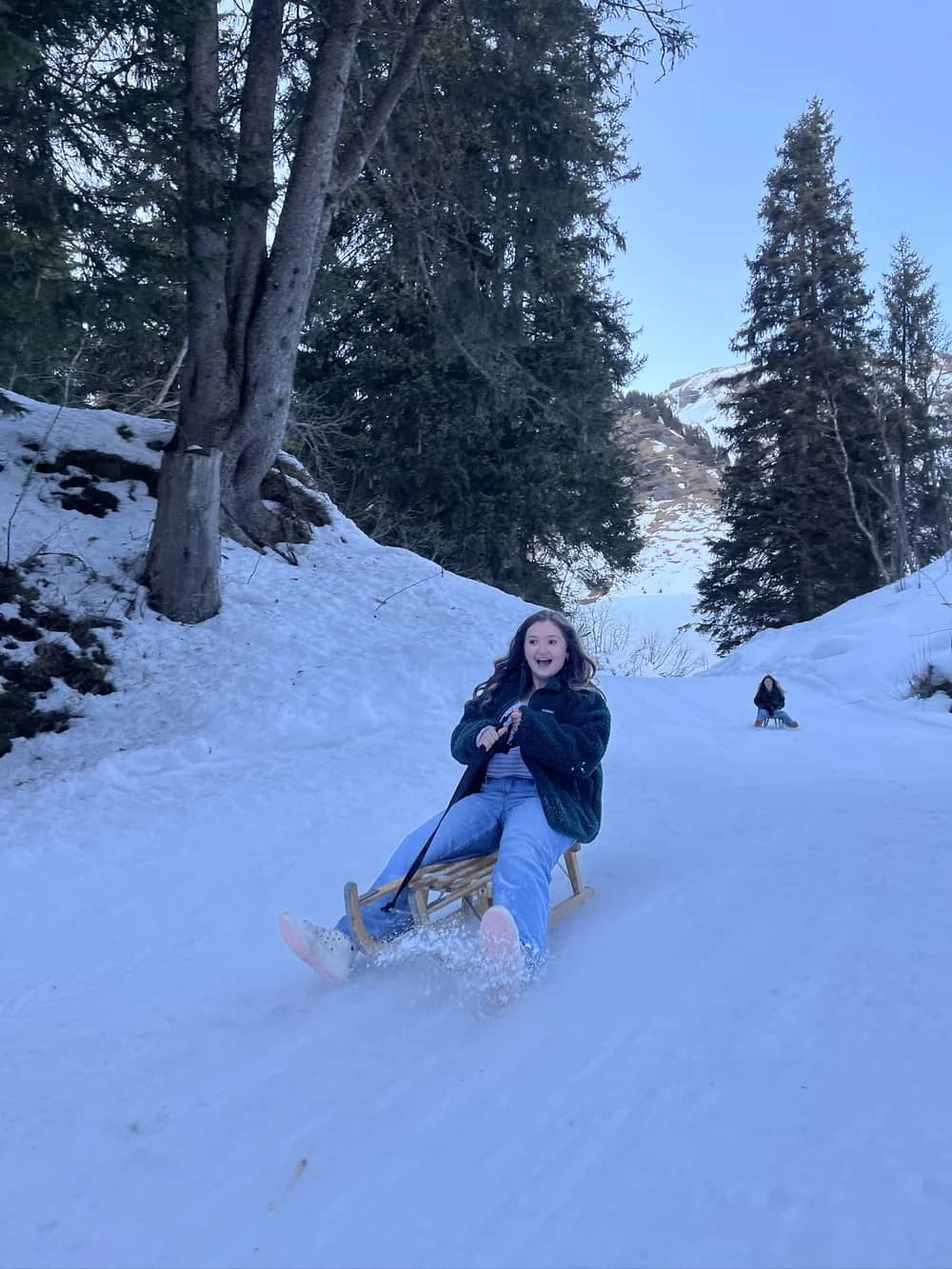 Ein Gast lenkt einen Holzschlitten mit einem Schuh im stiebenden Schnee auf der Schlittelbahn im Wald oberhalb von Mürren