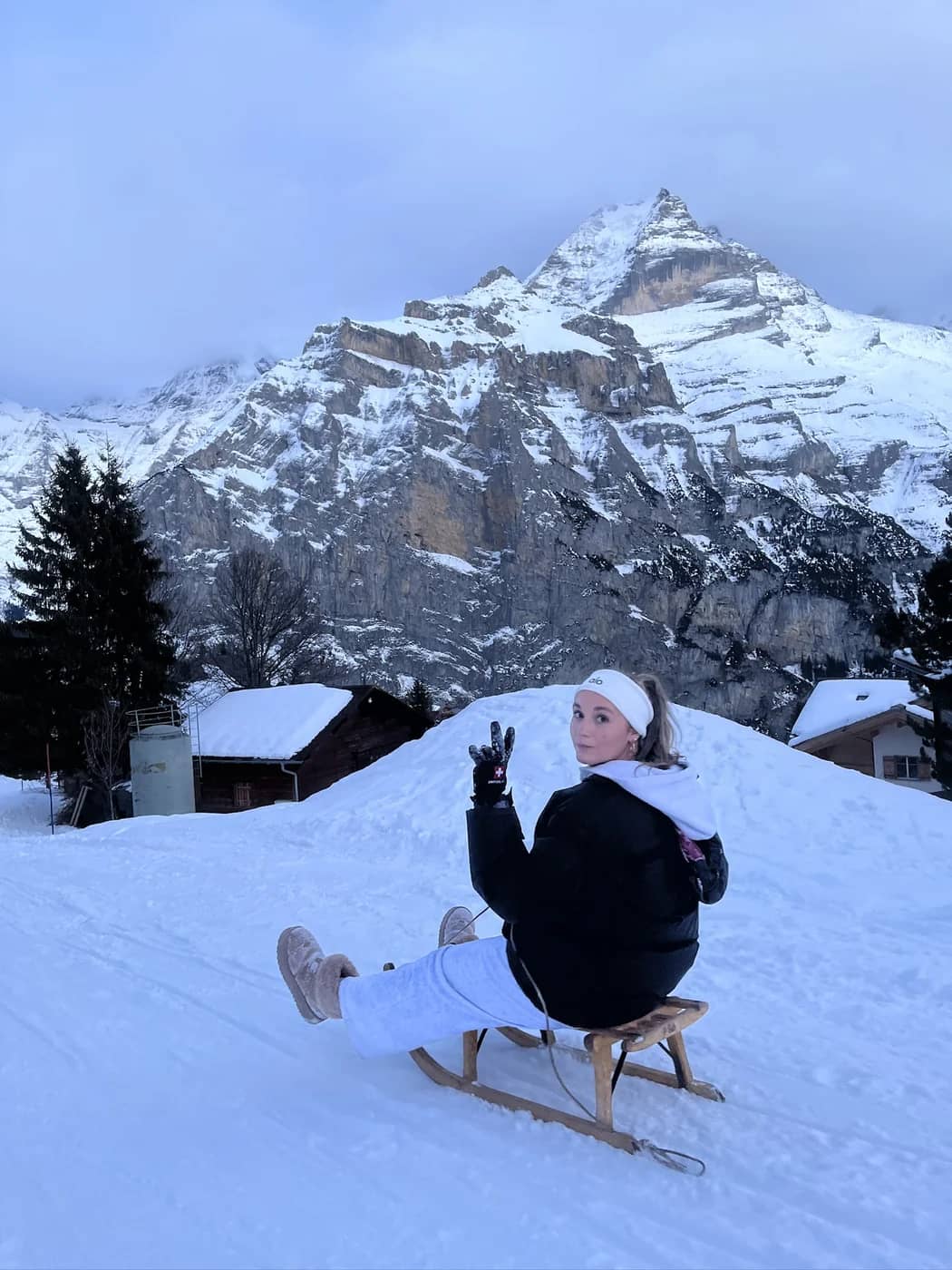 Ein Gast winkt von einem Davoser Holzschlitten unter einem verschneiten Felsgipfel am Start der Schlittelbahn in Mürren