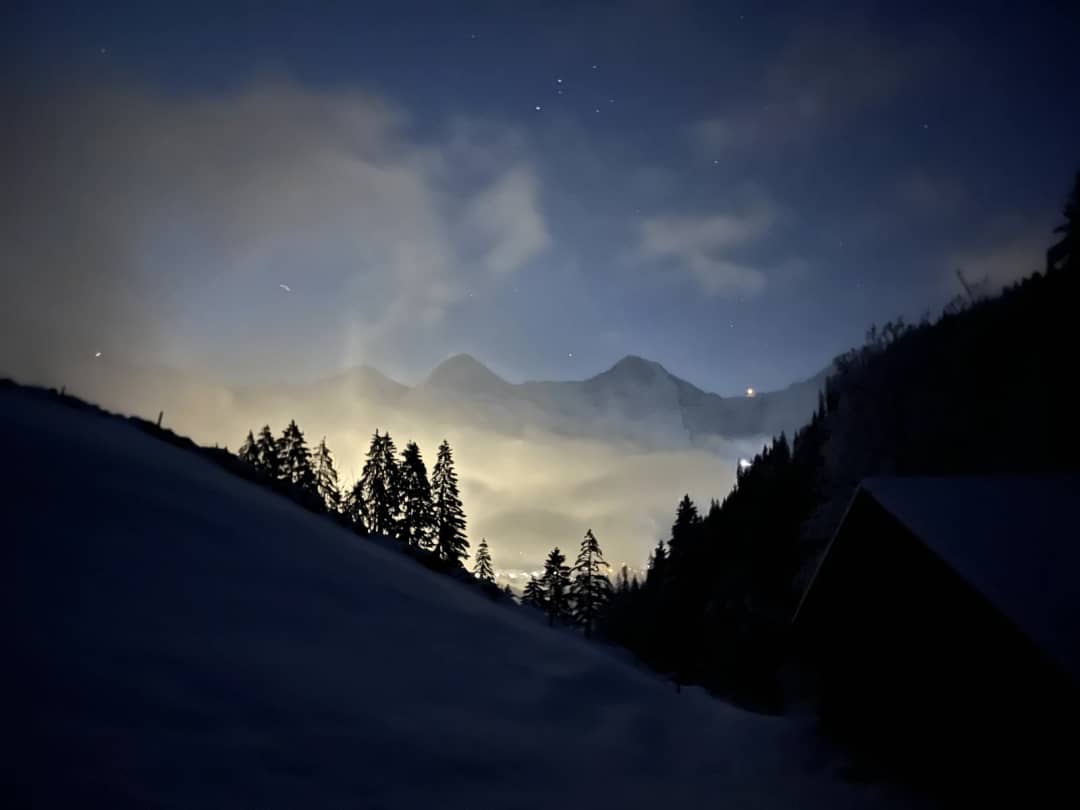 Nachthimmel und leuchtende Wolken über dem Lauterbrunnental, gesehen vom dunklen Hang der Schlittelbahn von Isenfluh