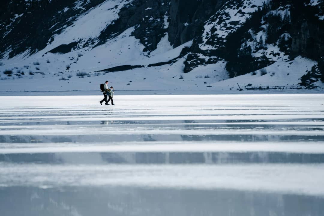 Zwei Wanderer queren den gefrorenen See unter verschneiten Felsen, der Oeschinensee im Winter bei Kandersteg