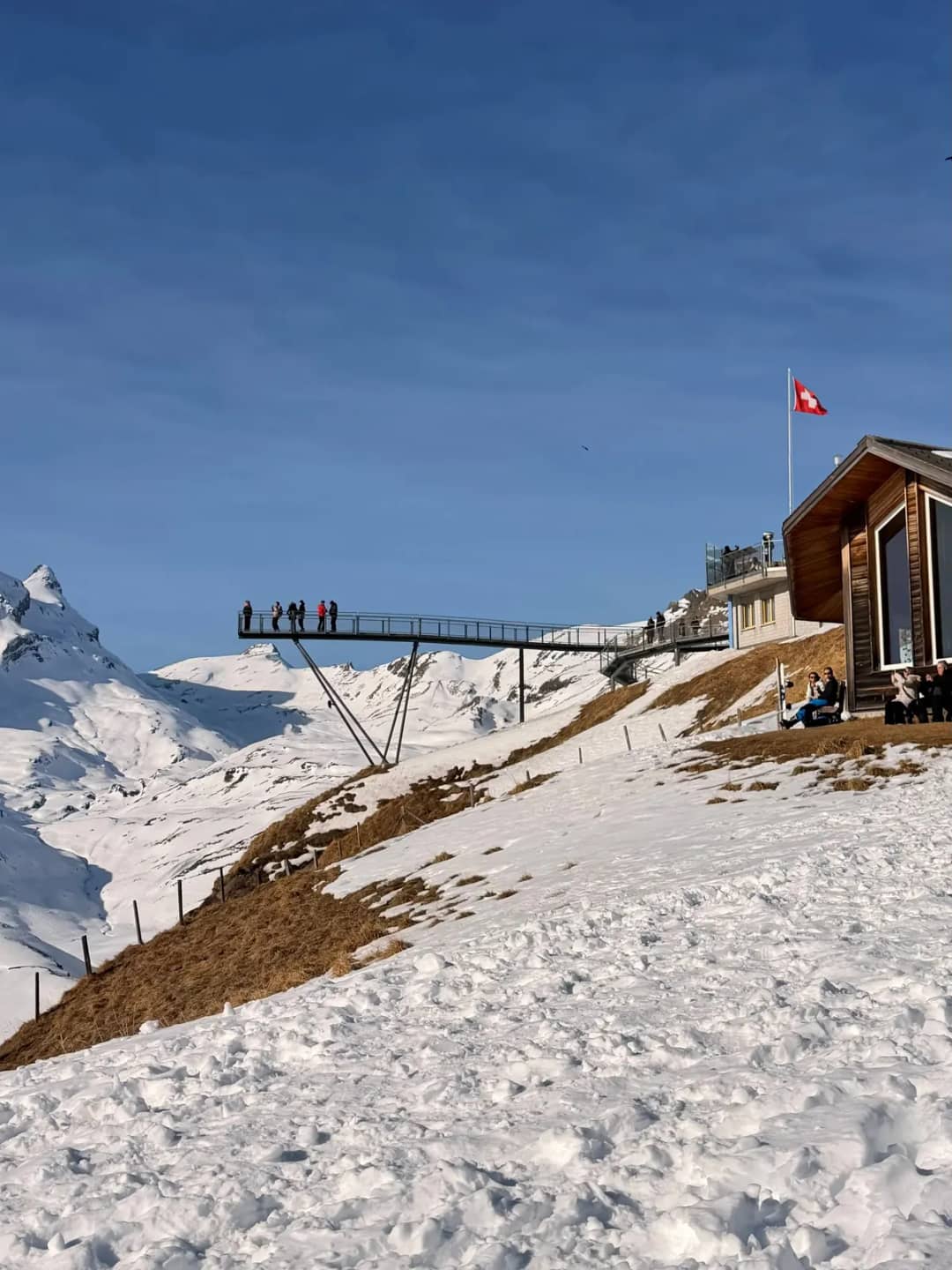 Der First Cliff Walk ragt an einem Januartag unter blauem Himmel aus einem verschneiten Hang über Grindelwald