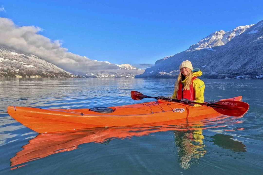 Kayakista con traje seco amarillo en un kayak naranja sobre el lago de Brienz en calma, bajo cumbres nevadas