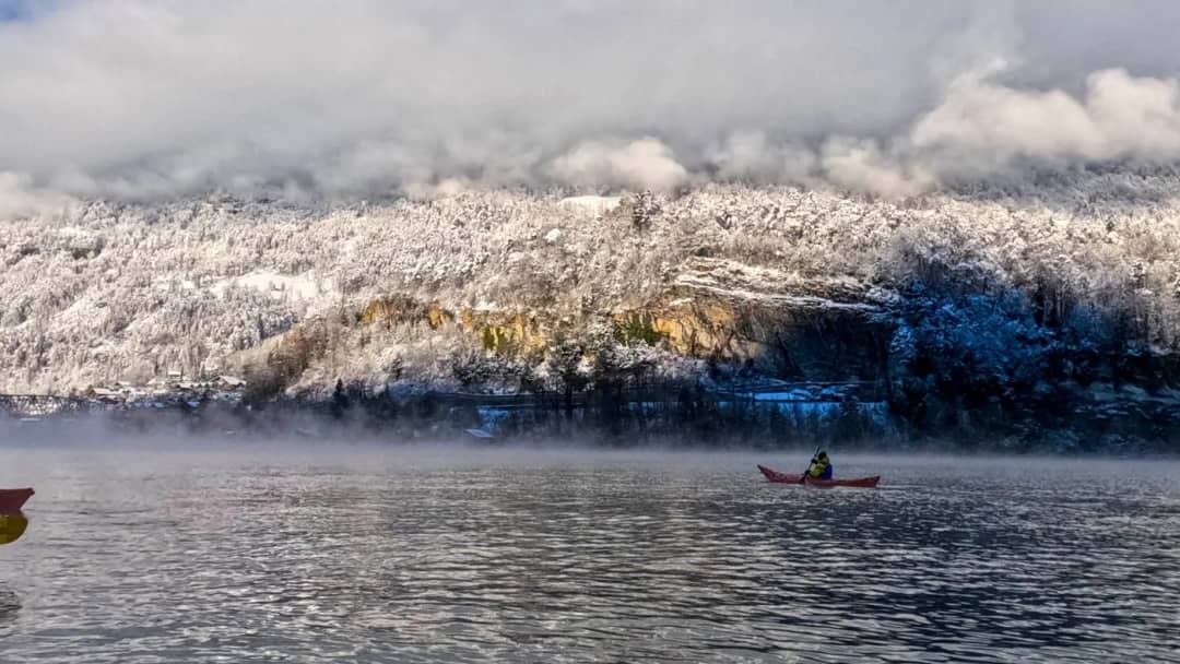 Kayakistas con traje seco y chaleco de flotación junto a un kayak rosa en el lago de Brienz, en invierno