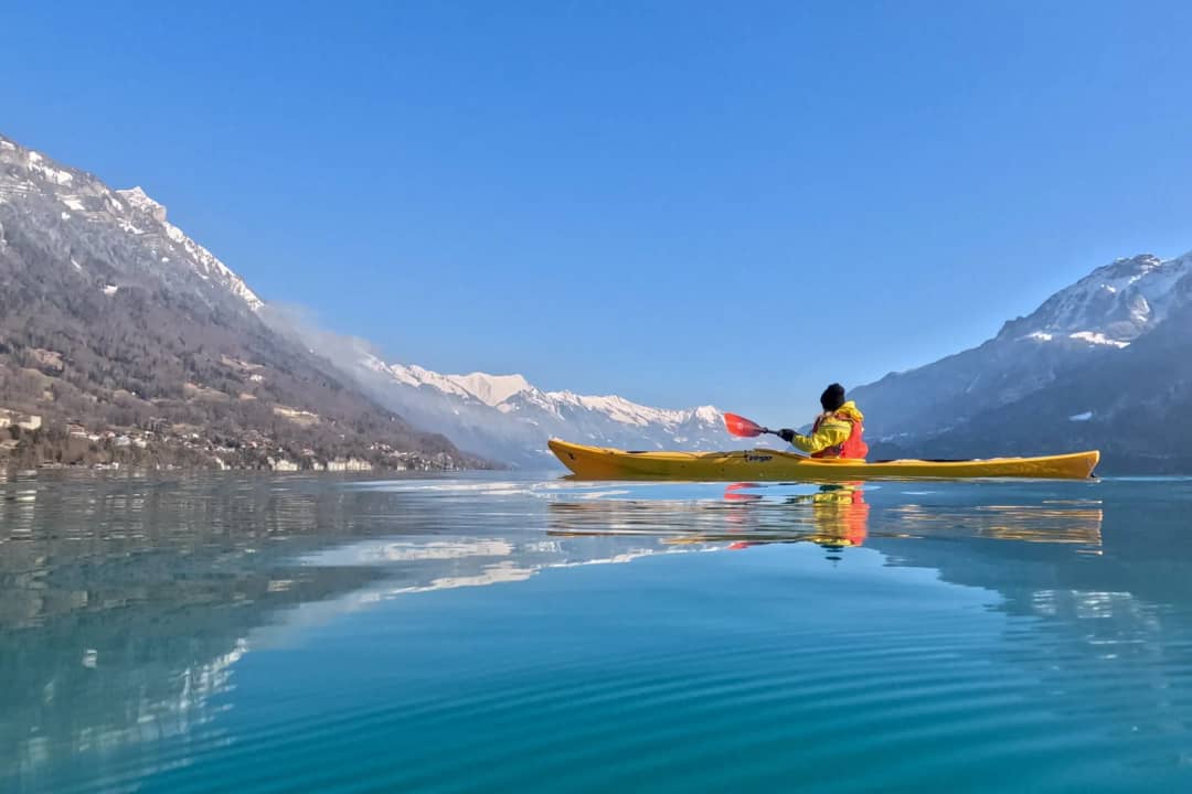 Kayakista solo en el lago de Brienz, liso como un espejo bajo montañas nevadas, al ritmo lento del invierno