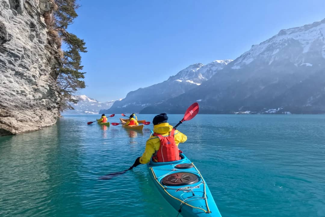 Kayakista en un kayak azul bajo un acantilado del lago de Brienz, con cumbres nevadas en un tour de invierno