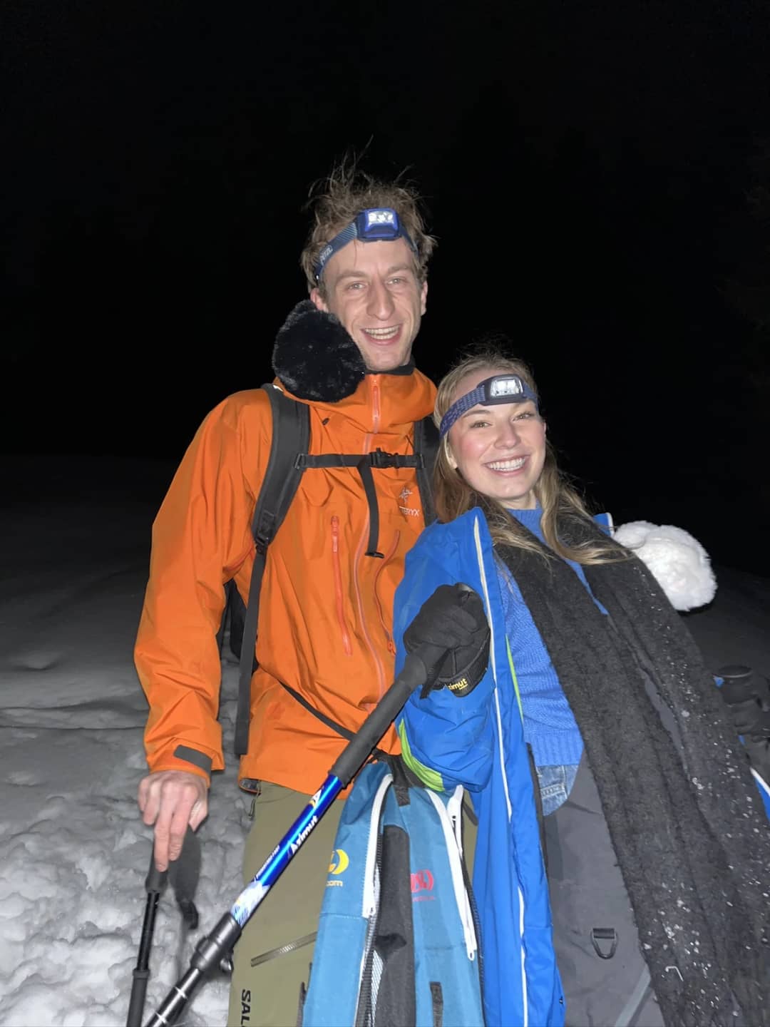 Pierre and a guest with headlamps and snowshoes on their backs smile on a snowy trail above Isenfluh at night