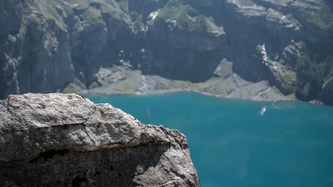 Saliente de roca caliza en primer plano sobre el agua turquesa del Oeschinensee, acantilados y pedregal abajo