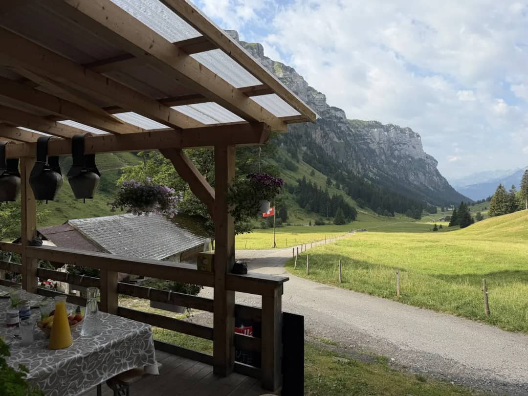 Terrasse couverte d'un alpage avec table de petit-déjeuner et cloches, vue sur la vallée du Justistal