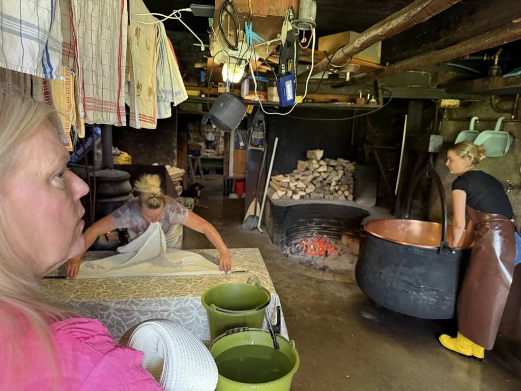 Copper cauldron on the wood fire of a Justistal alp dairy while a cheesemaker folds the cloth on the table