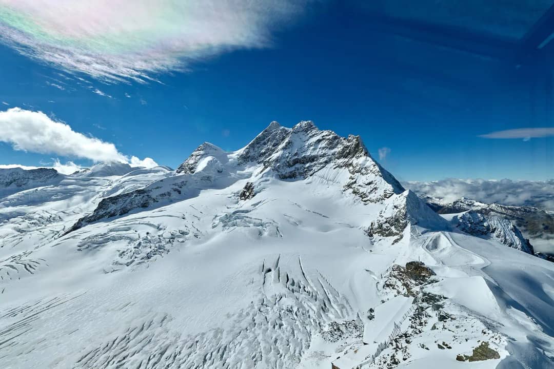 Snow-covered Jungfrau summit above a crevassed glacier, seen from the Sphinx at Jungfraujoch, deep blue sky.