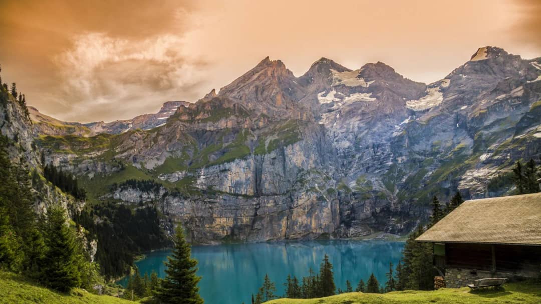 Holzhütte über dem türkisfarbenen Oeschinensee bei Sonnenuntergang, hohe Felswände hinter dem Bergsee