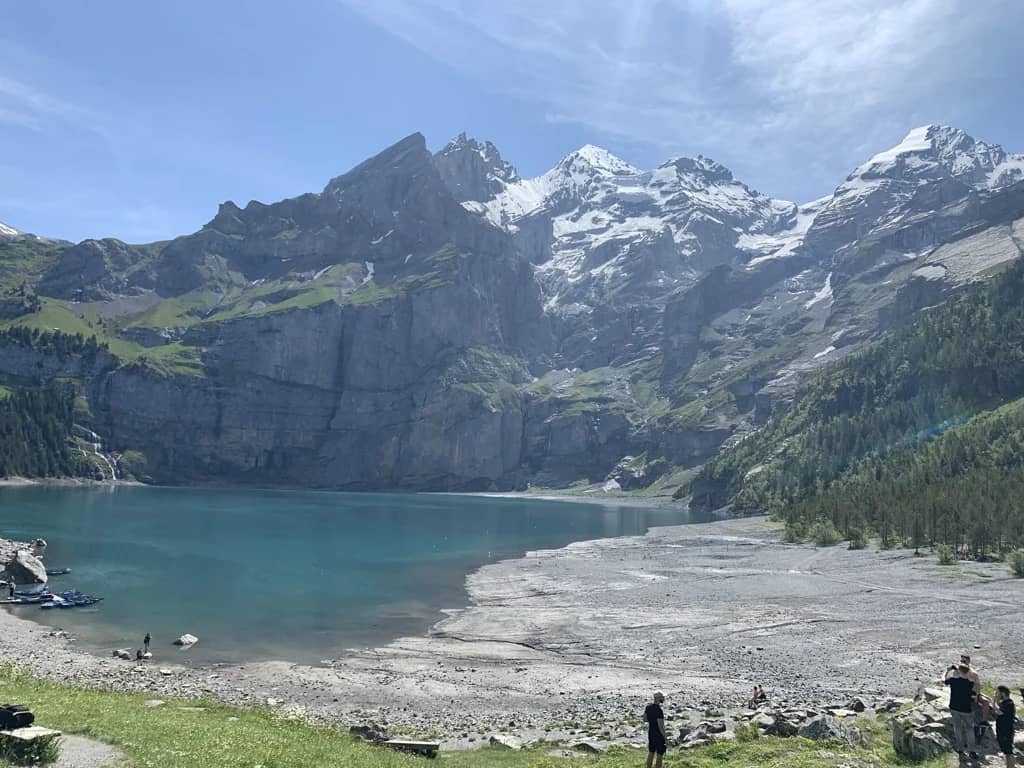 Eaux turquoise de l'Oeschinensee sous les falaises et les sommets enneigés, visiteurs sur la rive de galets