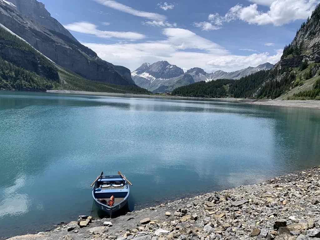 Blaues Ruderboot am steinigen Ufer des Oeschinensees, milchig türkisfarbenes Wasser und Felswände beidseits