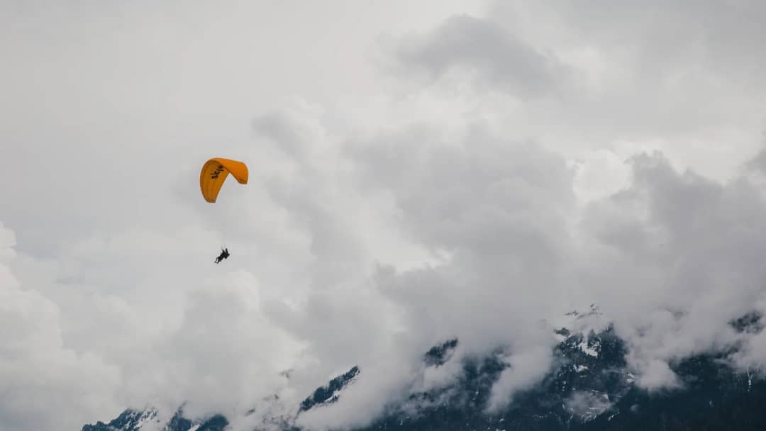 Orange tandem paraglider drifting through heavy cloud above snow-dusted slopes near Interlaken, Switzerland