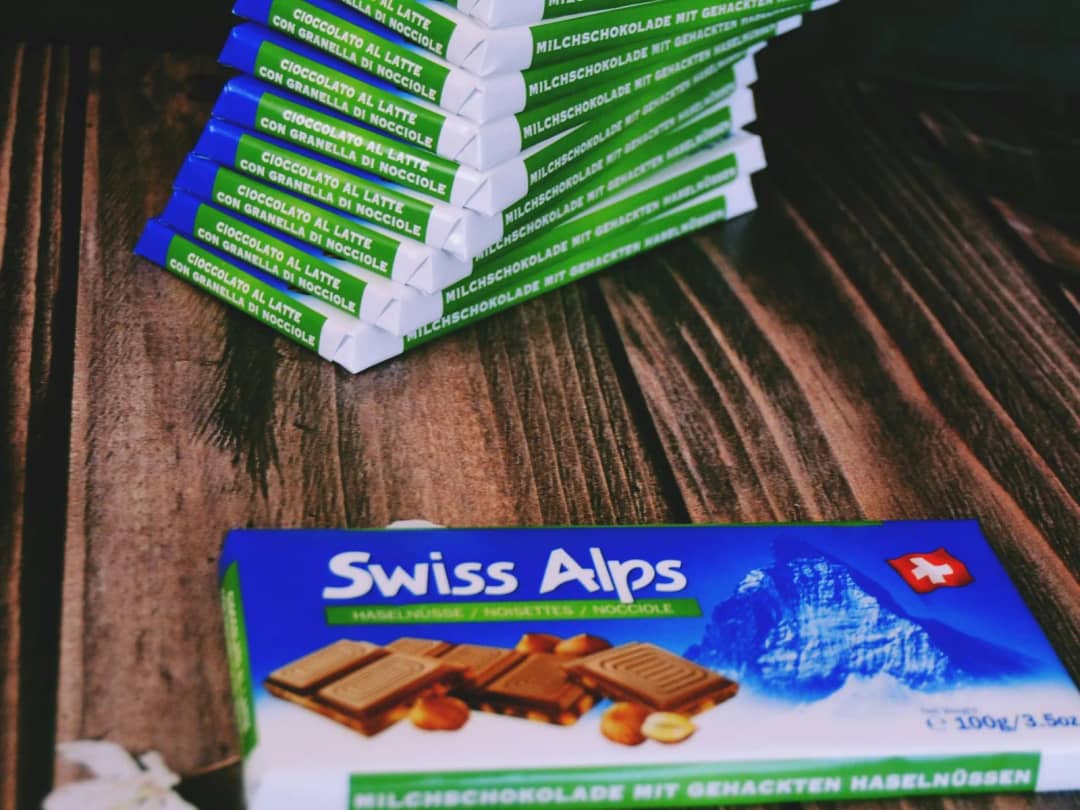 Stapel Swiss Alps Milchschokolade mit Haselnüssen auf einem Holztisch, eine Tafel liegt flach davor im Bild