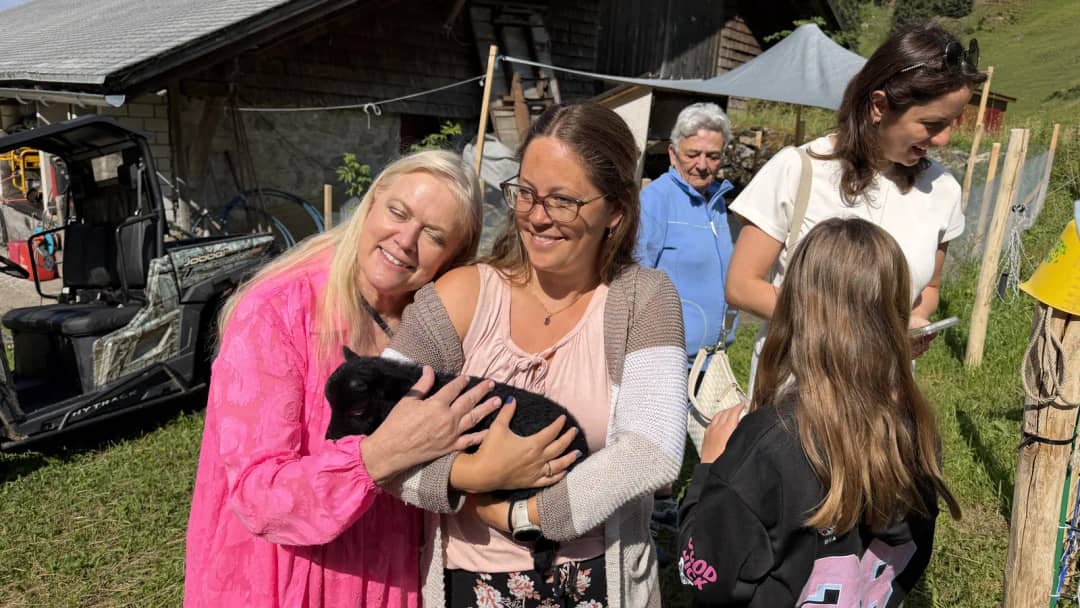 Deux clientes du Farm Tour sourient en serrant un chevreau noir devant une grange de la vallée du Justistal