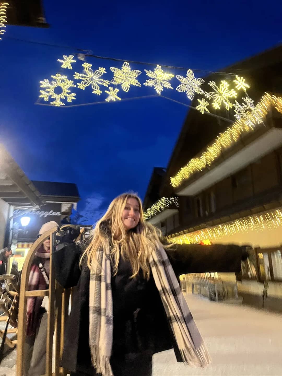 Cliente sostiene un trineo de madera bajo luces de Navidad en el pueblo de Mürren al anochecer, tras la Bob Run