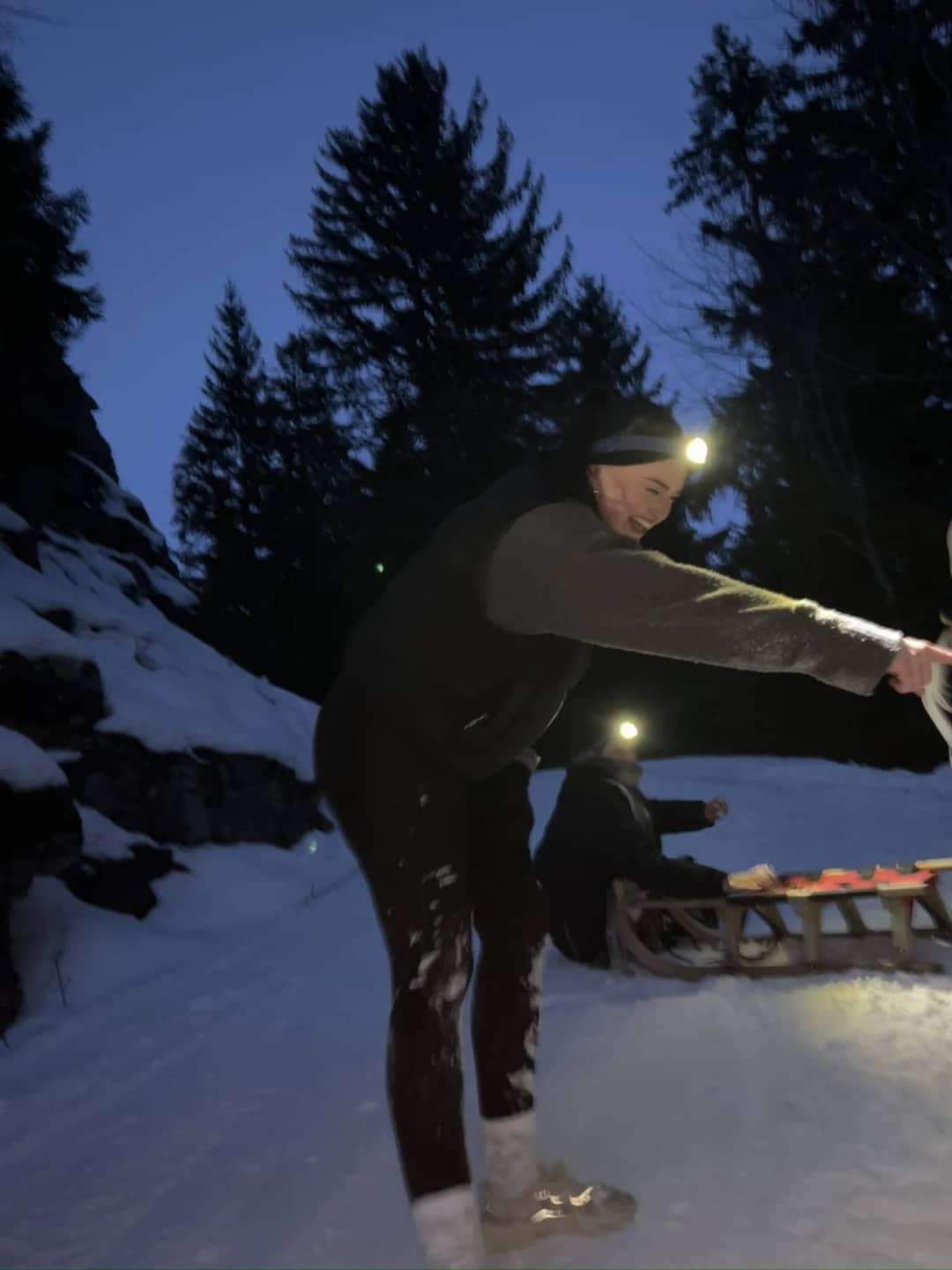 Clientes con linternas frontales al anochecer en el camino nevado del bosque sobre Isenfluh, cae la oscuridad