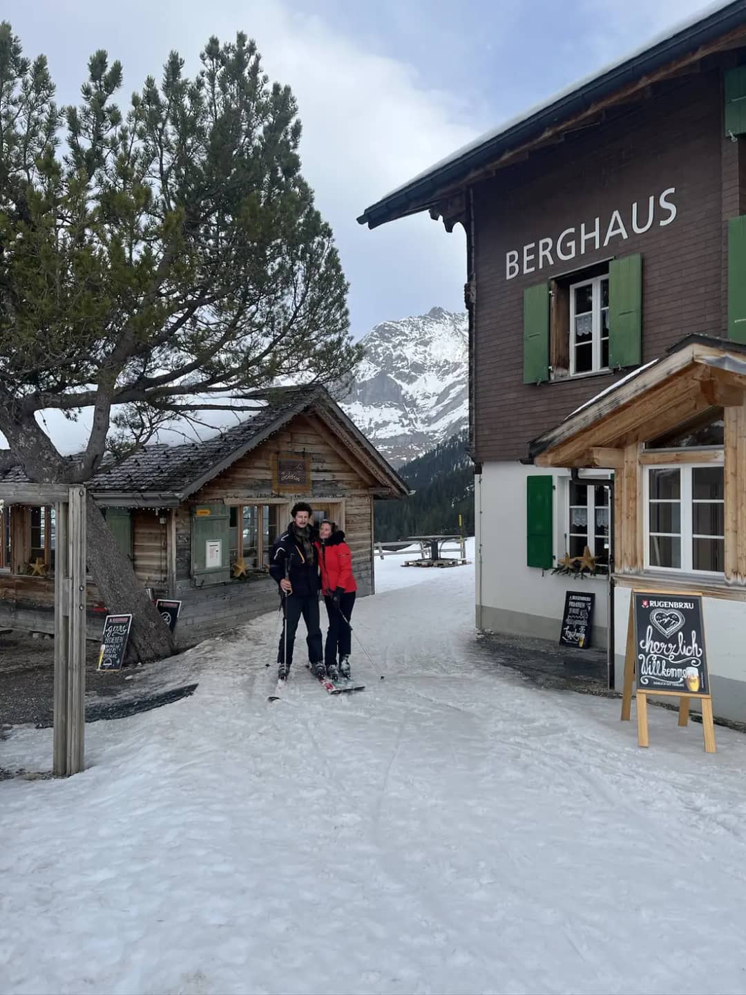 Two winter walkers in front of the Berghaus at Alpiglen above Grindelwald, snow on the path and fir trees behind