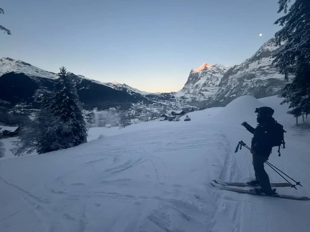 Skier on a shaded slope above Grindelwald as the peaks at the head of the valley glow pink in December
