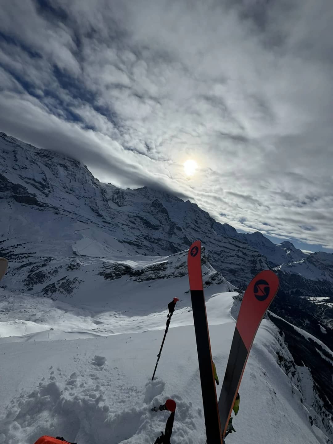 Pair of skis planted in deep snow in the Männlichen ski area, the winter sun behind thin clouds over the peaks
