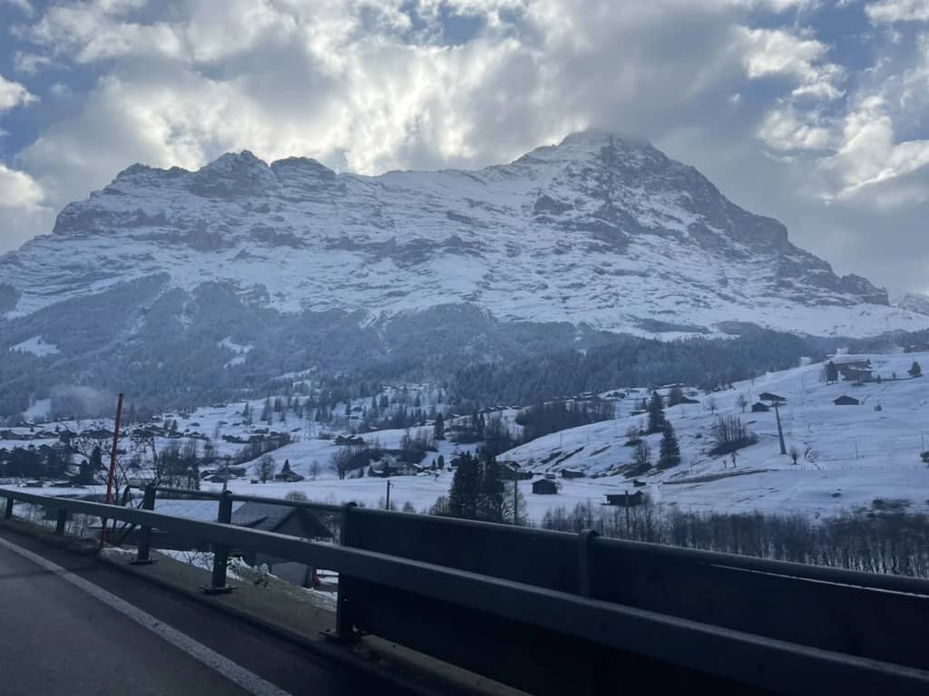 Snowy peaks and white meadows seen from the road into Grindelwald on a December morning, clouds over the summit