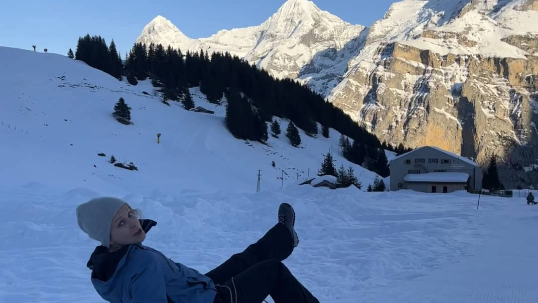 Sledder lying back in the snow at the Allmendhubel above Mürren, sunlit peaks behind on a February evening