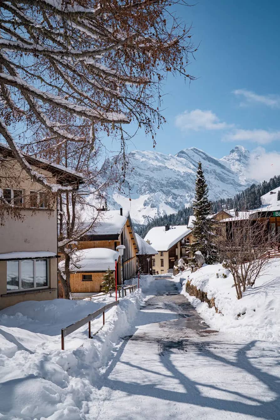 Narrow snowy lane between traditional chalets in Mürren with the Bernese Alps behind on a winter day