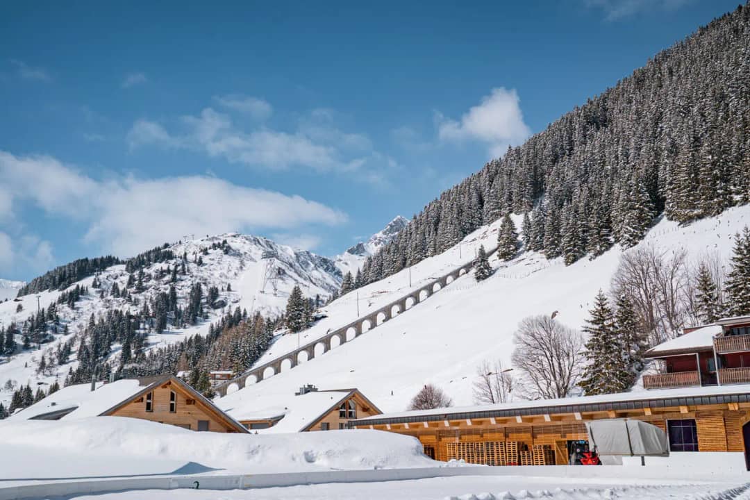 Allmendhubel funicular bridge on the snowy slope above Mürren with chalet roofs and fir forest in winter