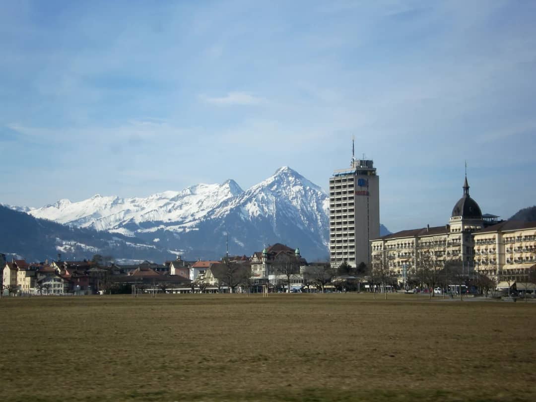 Bare winter grass of the Höhematte in central Interlaken in February, with hotels and the snowy Niesen behind