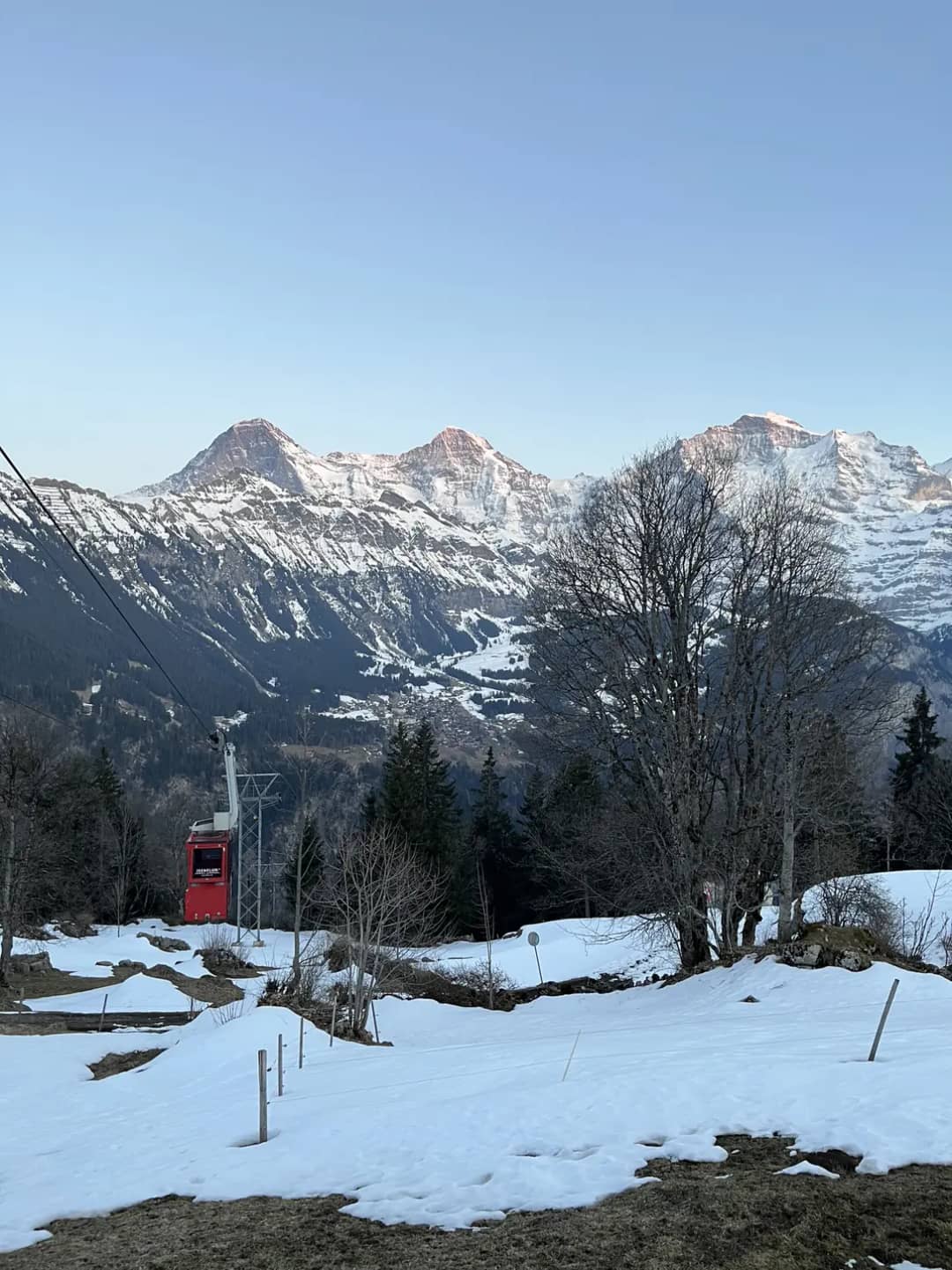 Eiger, Mönch and Jungfrau above the red Sulwald cable car and the snowy meadows of Isenfluh on a March evening
